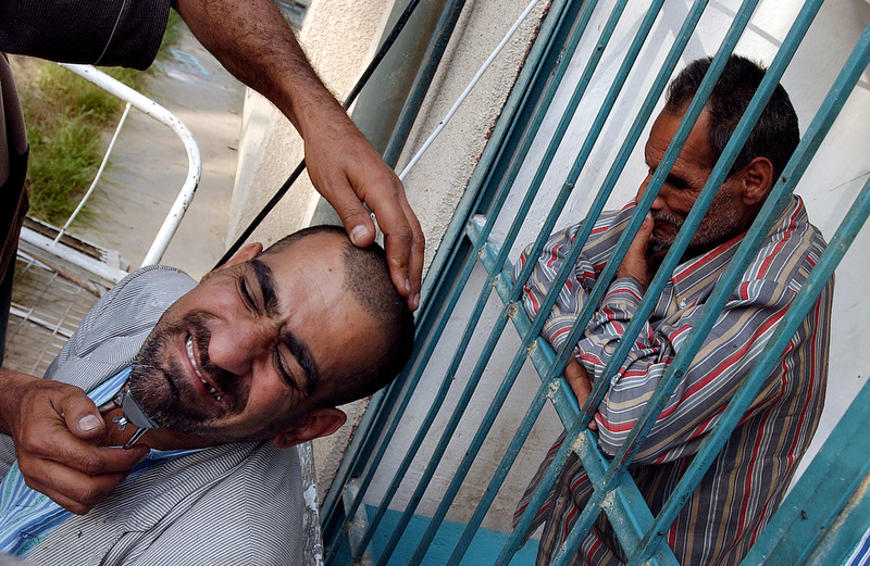 A patient receives a shave from a hospital staff member while another patient waits behind the bars. The hospital was run by the government but is now run by a Shiite charitable organization. The provide care with few resources under desperate conditions after the fall of Saddam's government.