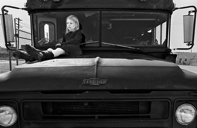 Left alone by their parents for the afternoon, Zoe sits on the hood of the bus.